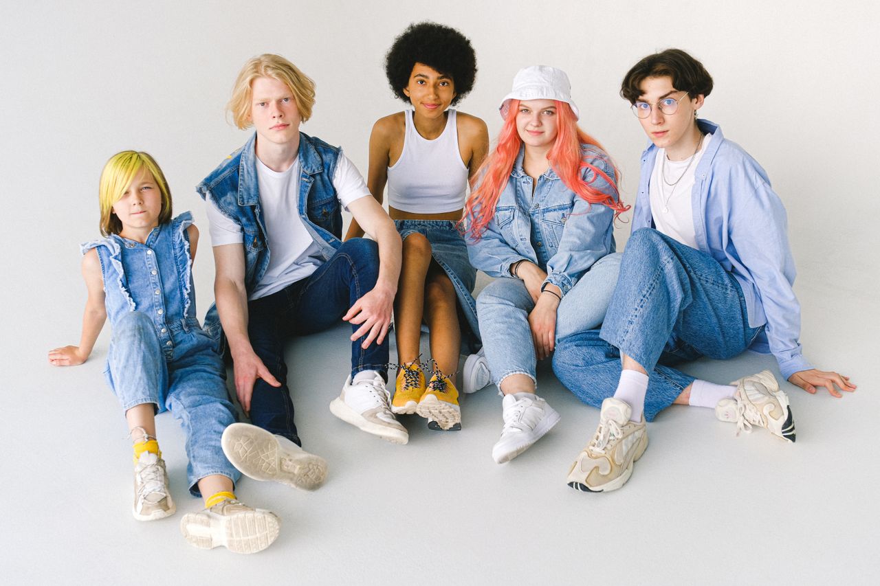 From above of full body group of smiling teenager friends sitting on floor against white background and looking at camera
